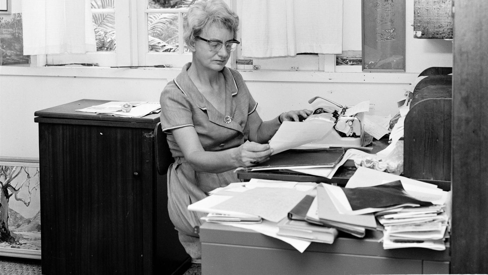 Woman at a desk with a typewriter, looking at papers
