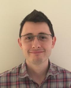 A head shot of Dr Rohan Howitt against a bare wall. He is wearing a checked shirt.