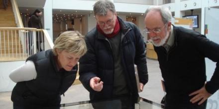 A photograph of Dr Christine Hansen, Dr Mike Smith (centre), and Prof. Tom Griffiths examining artefacts.
