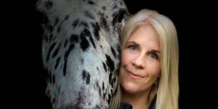 Professor Sandra Swart is pictured next to her horse, which is white with black spots. They are both looking at the camera.
